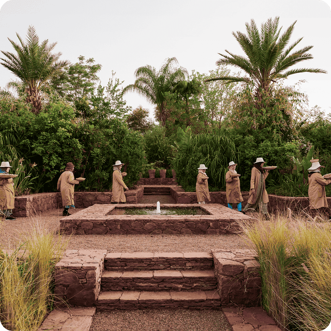 2026luxedivisionbrandyslbeautywomenwearingbiegecoatandhatandwalkingaroundwaterfountain