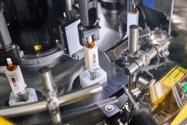 Produktionsmaschine mit drei weißen Verpackungsflaschen in der Befüll- oder Etikettierstation.