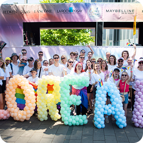 Die Mitarbeitenden von Loreal stehen vor ihrem CSD Wagen hinter Luftballons in Regenbogenfarben die das Wort Loreal ergeben