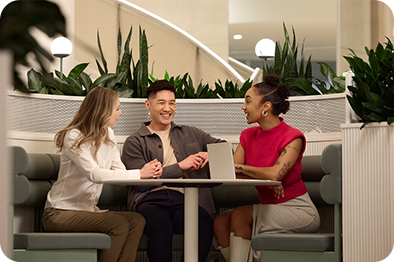 Zwei Kolleginnen und ein Kollege sitzen bei der Arbeit und unterhalten sich