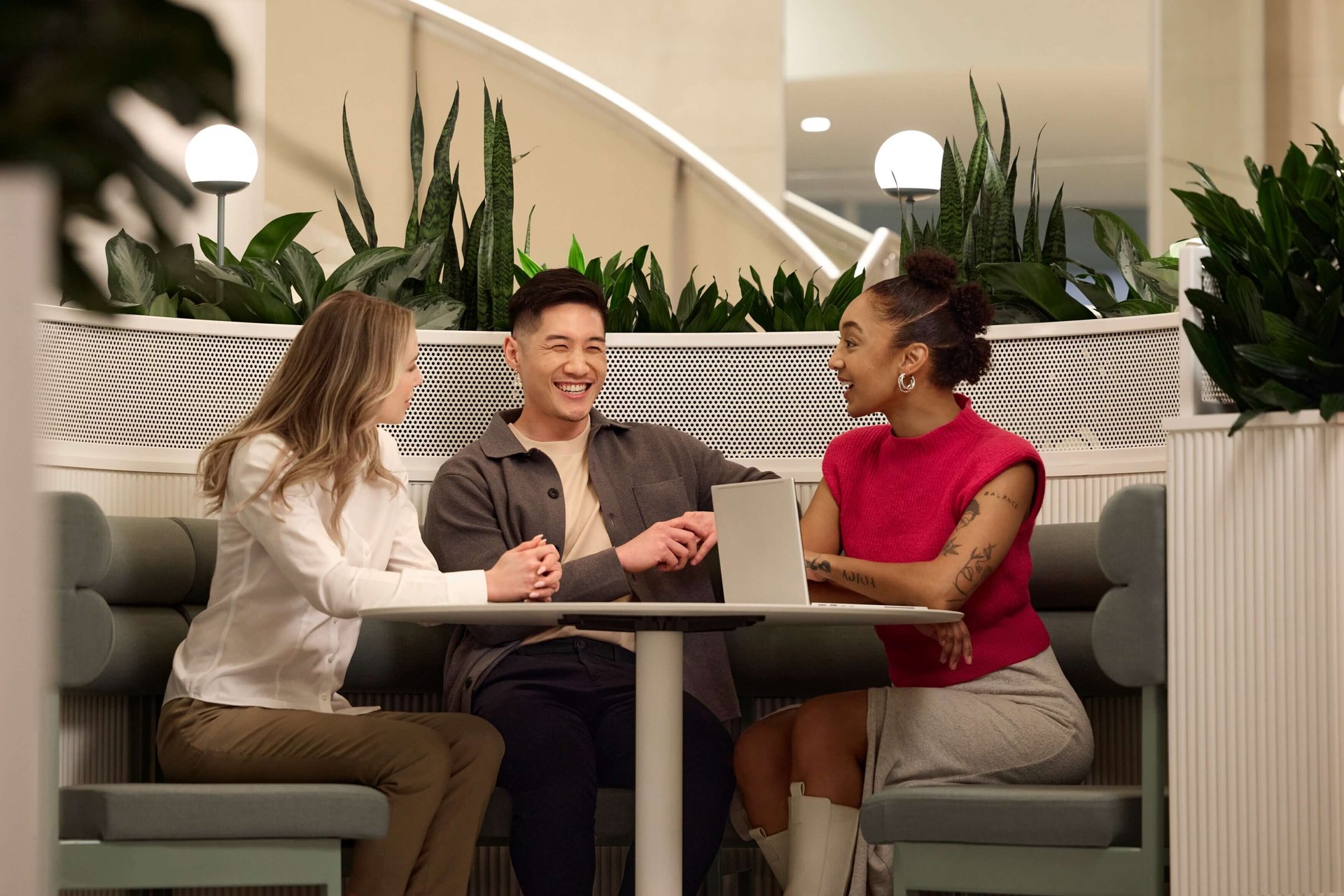 Drei Studierende sitzen an einem Tisch mit Laptop und tauschen sich aus