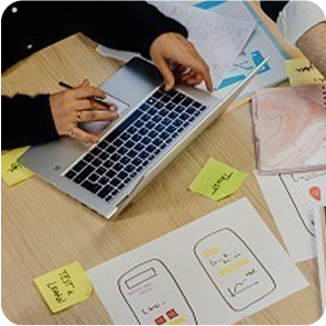 Nahaufnahme von einem Tisch auf dem Papiere liegen und an dem jemand sitzt und arbeitet