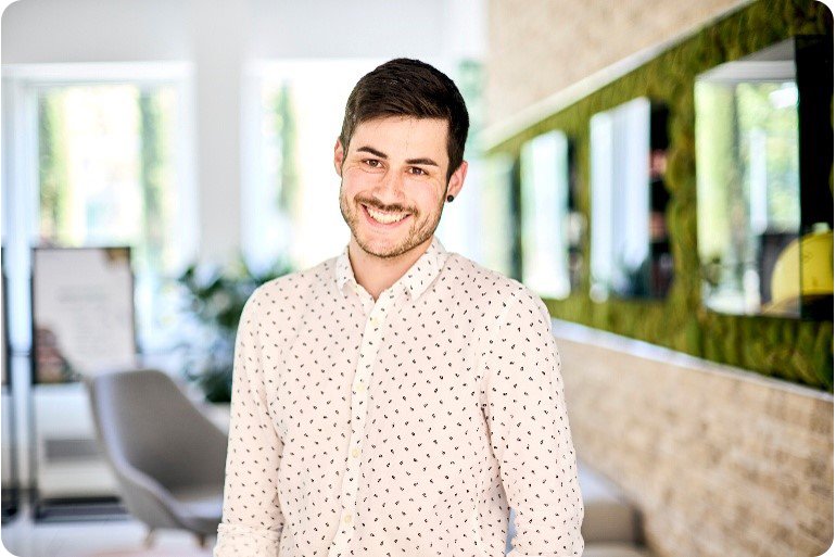 Ein junger Mann im Hemd steht lächelnd im Büro