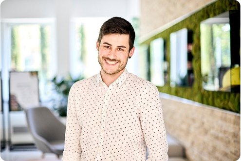 Ein junger Mann im Hemd steht lächelnd im Büro
