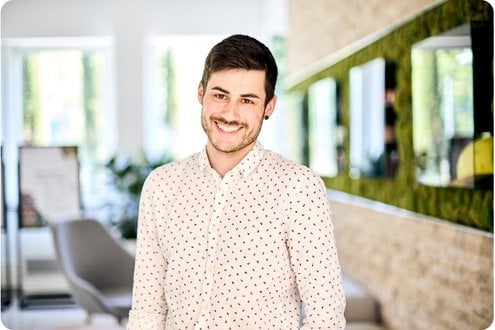 Ein junger Mann im Hemd steht lächelnd im Büro